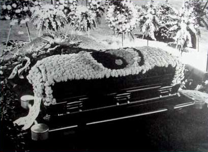 Une photo en noir et blanc d'un cercueil orné de fleurs, capturant la solennité de la mort de Bruce Lee.